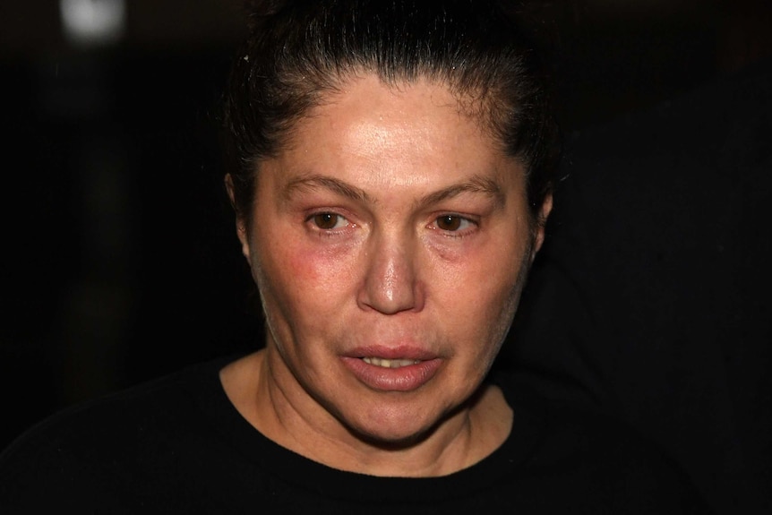 A close-up of Roberta Williams's face in the dark, with her looking serious.