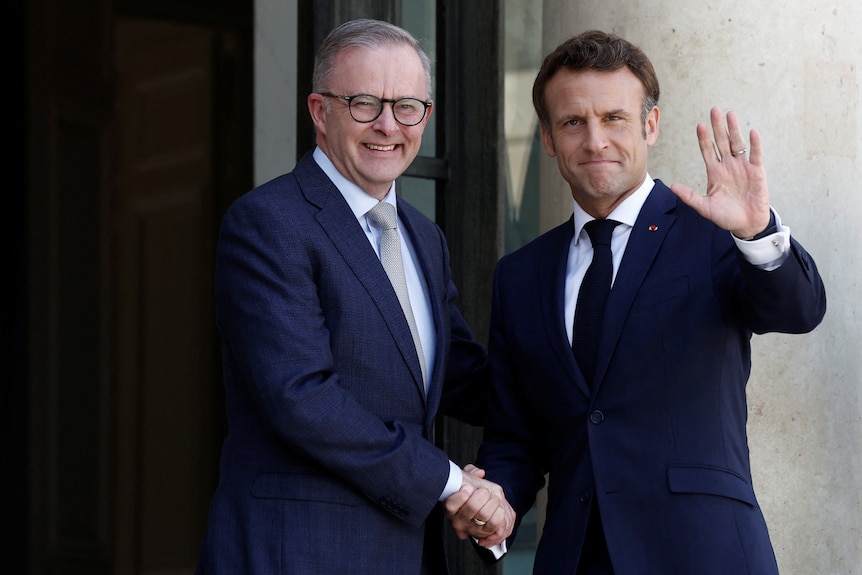 Two men shake hands for camera as one waves.