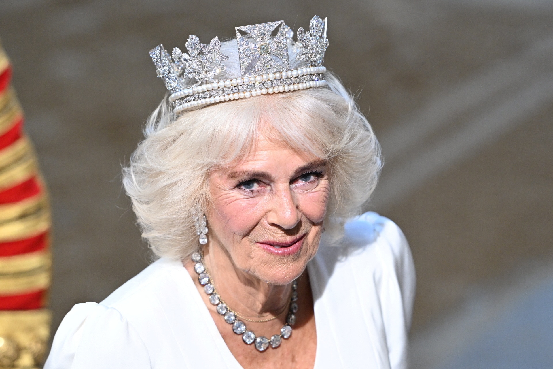 Queen Camilla wearing a jewel crown and jewel necklace in a white dress
