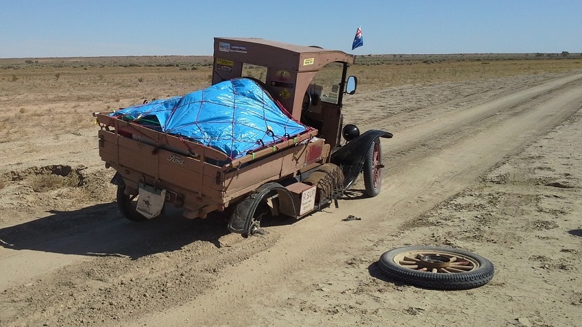A vintage car stuck on an outback dirt road because a wheel has fallen off.