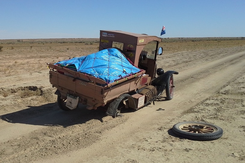 A vintage car stuck on an outback dirt road because a wheel has fallen off.