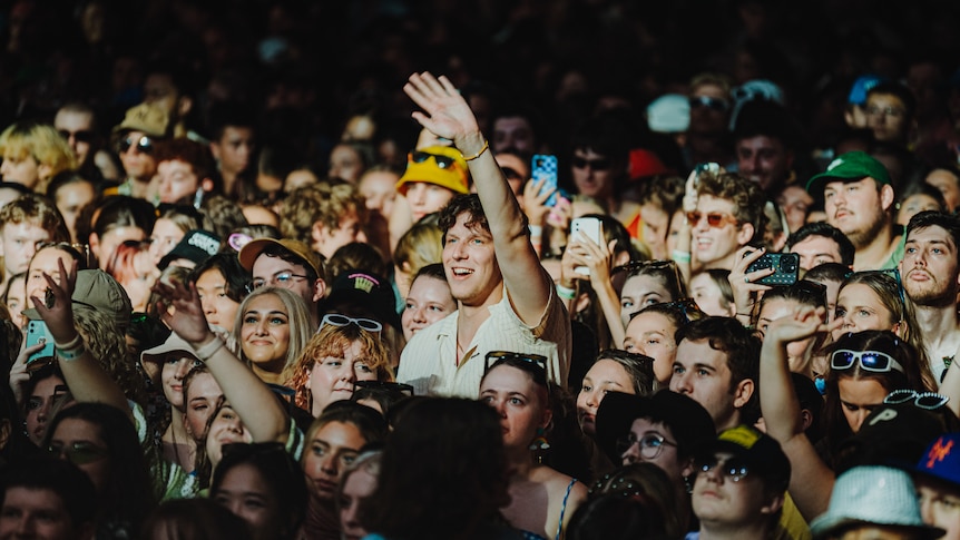 A young man in a massive crowd puts his hands in the air as he enjoys a live music performance