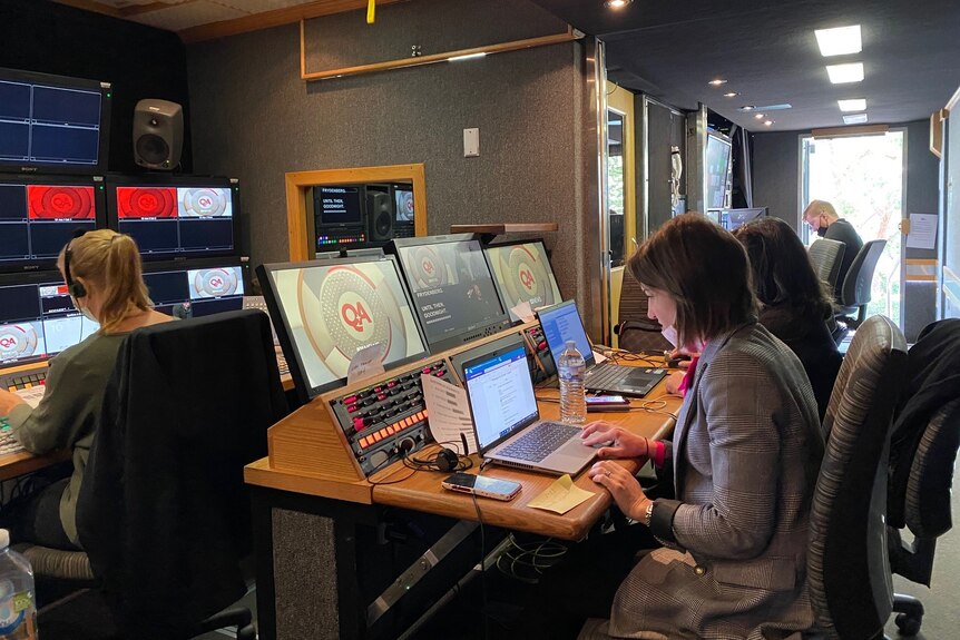 Woman sitting at desk looking at a laptop in TV broadcast truck control room.