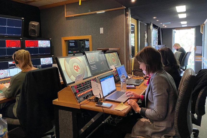Woman sitting at desk looking at a laptop in TV broadcast truck control room.