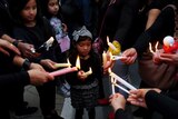 A young girl dressed in black is in the middle of a group of people who are holding candles together