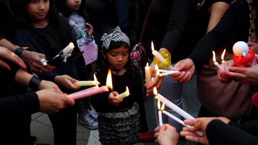 A young girl dressed in black is in the middle of a group of people who are holding candles together