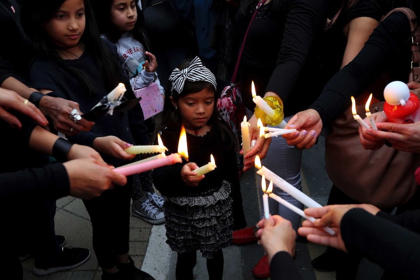 A young girl dressed in black is in the middle of a group of people who are holding candles together