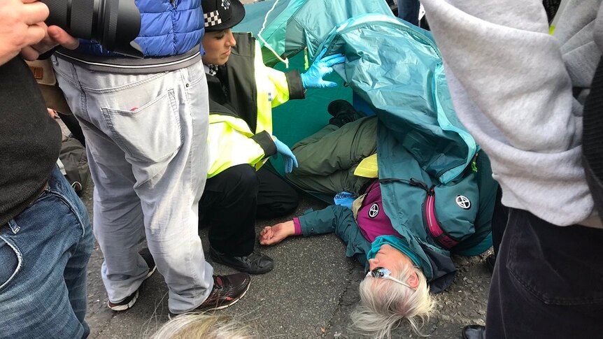 A police officer speaking to a protester lying on the ground in a green tent during the climate change protest in London.