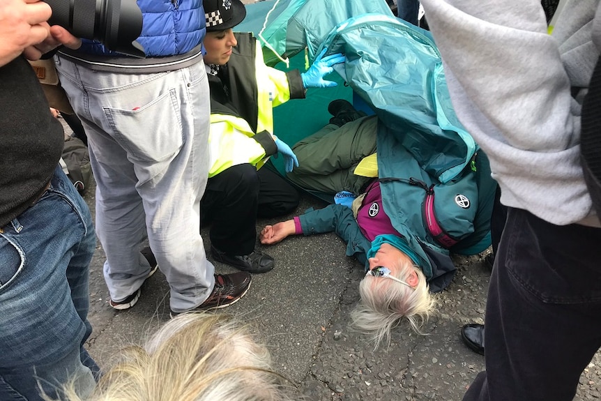 A police officer speaking to a protester lying on the ground in a green tent during the climate change protest in London.