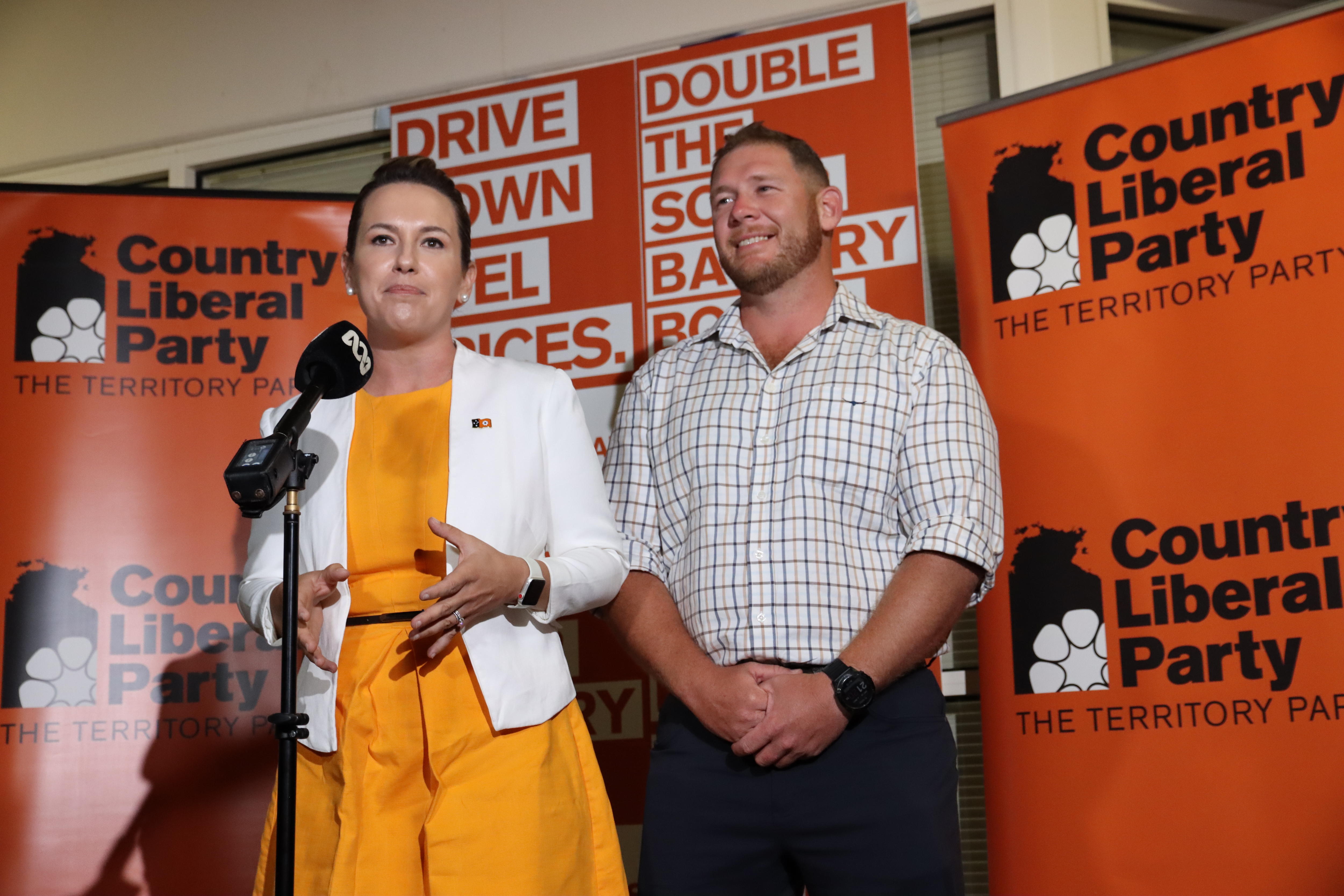 Lia Finocchiaro and Ben Hosking standing in front of a microphone looking at cameras.