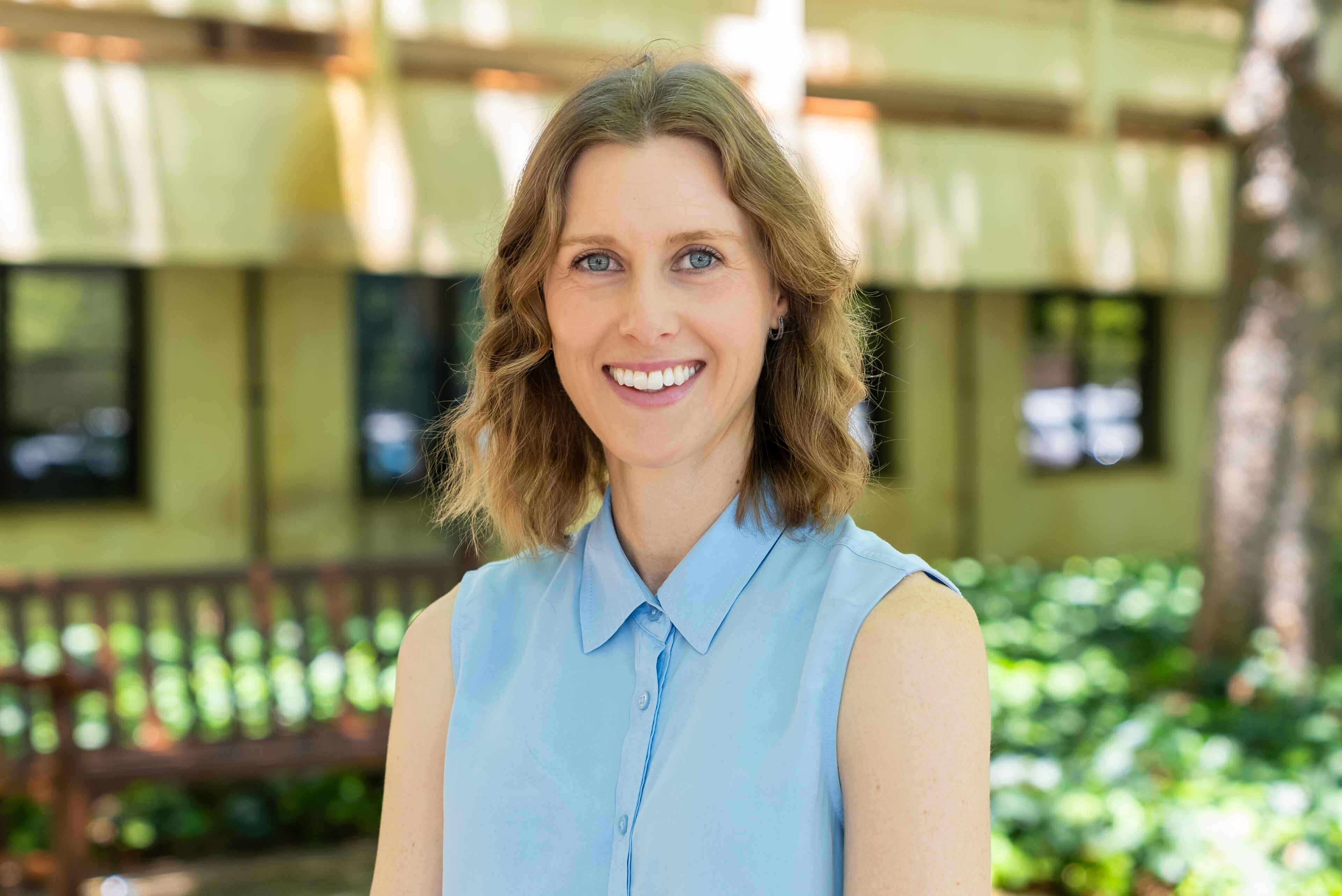 Short -haired woman with a blue shirt, smiling in front of the building