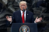 US President Donald Trump wearing a red tie gestures with open palms giving a rousing speech to the people of Warsaw.