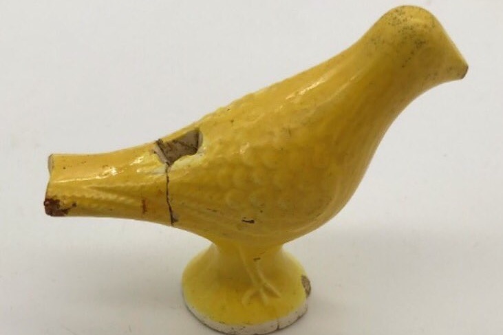 A close up photo of a yellow, bird-shaped whistle.