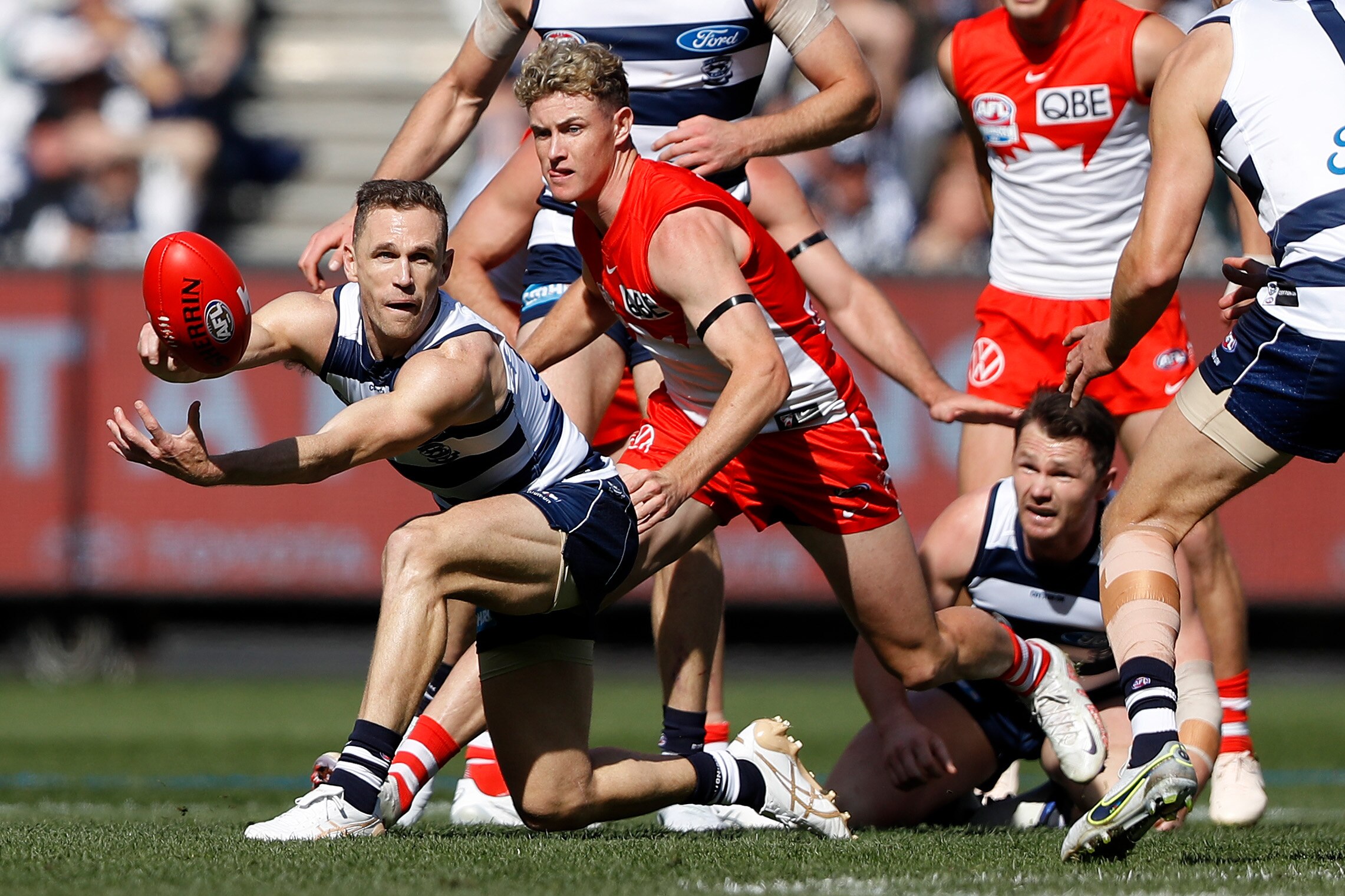 Joel Selwood gets a handball away while Swans players look to tackle him