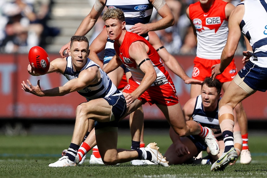 Joel Selwood gets a handball away while Swans players look to tackle him