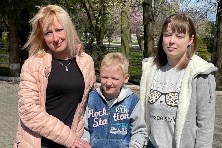 Ukrainian woman standing with her son, who is on a scooter, and her daughter.