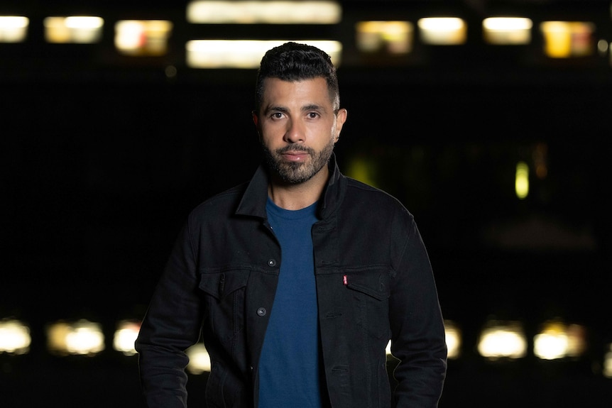 Night portrait of young man looking straight at the lens with blurred lights in background