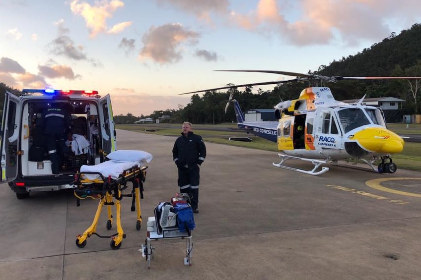 An ambulance and rescue helicopter at an airport as paramedics transport a man.
