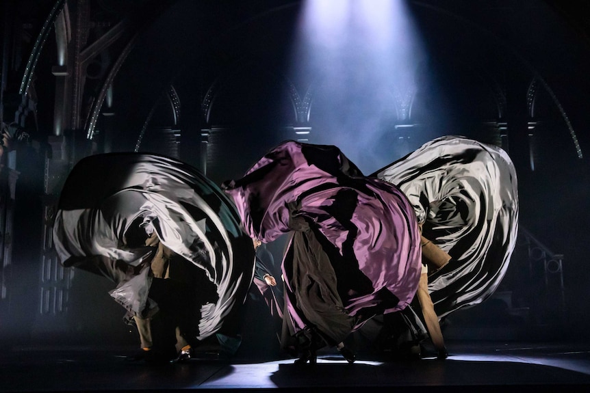 Three enormous cloaks swish in the air on stage