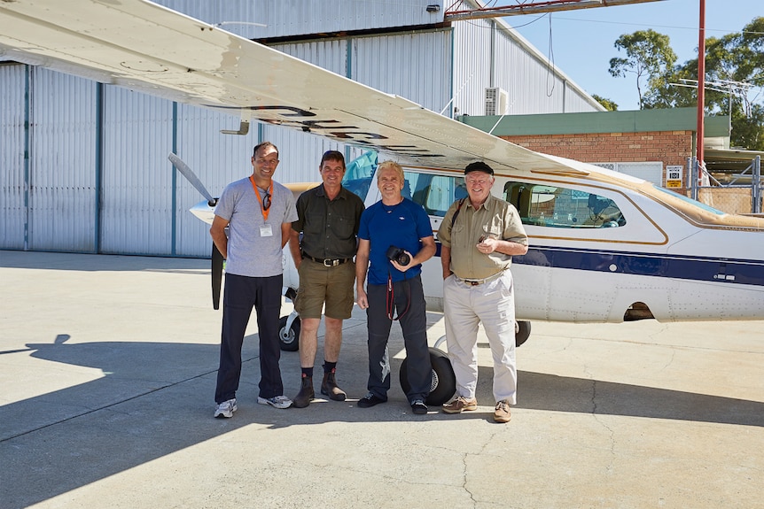 Four men standing in front of a small plane.