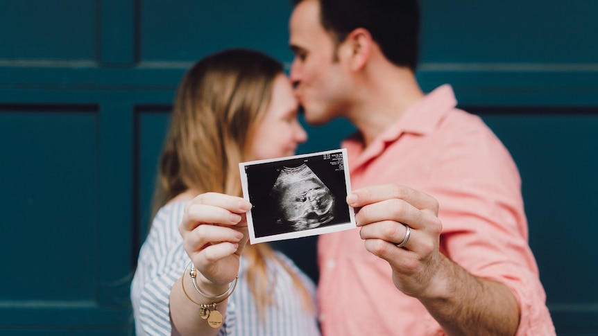 Couple hold ultrasound image of baby and kiss on the background in story about sharing photos of children online