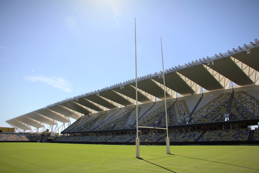 An empty grandstand overlooks a green football field on a sunny day