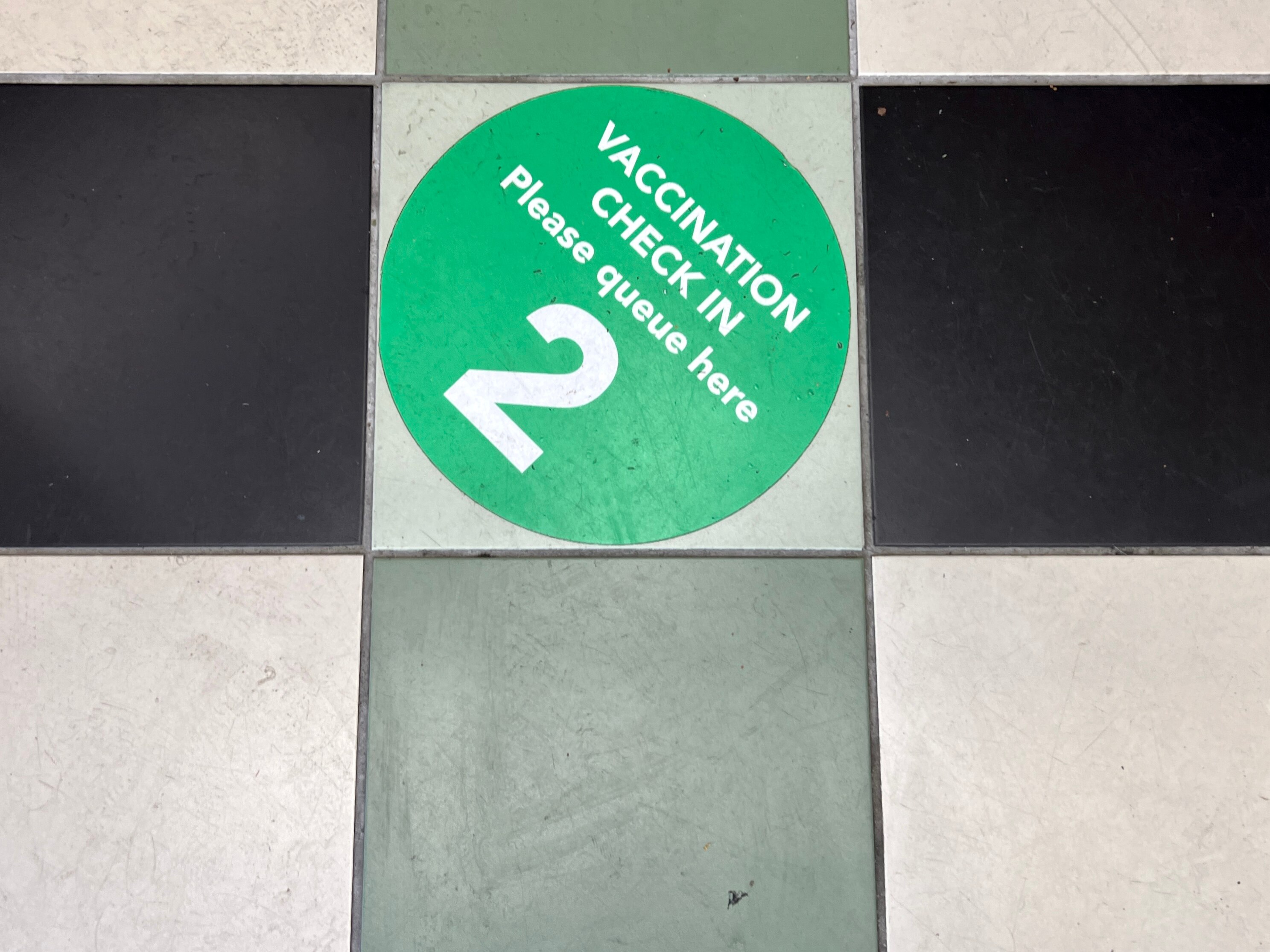 Faded social distance stickers on the footpath and people walking with masks as they pass hand sanitiser stations.