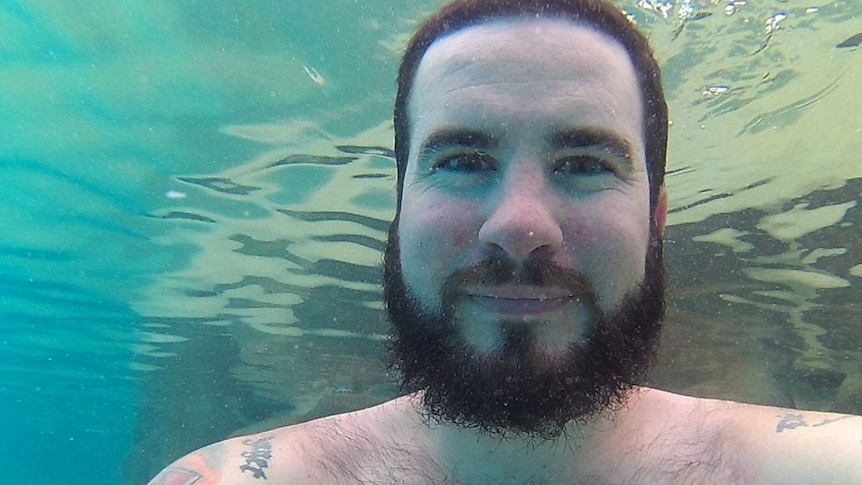A man smiles underwater at the camera