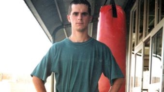 man in shirt and shorts standing in front of a punching bag