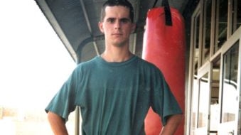 A man in shirt and shorts standing in front of a punching bag