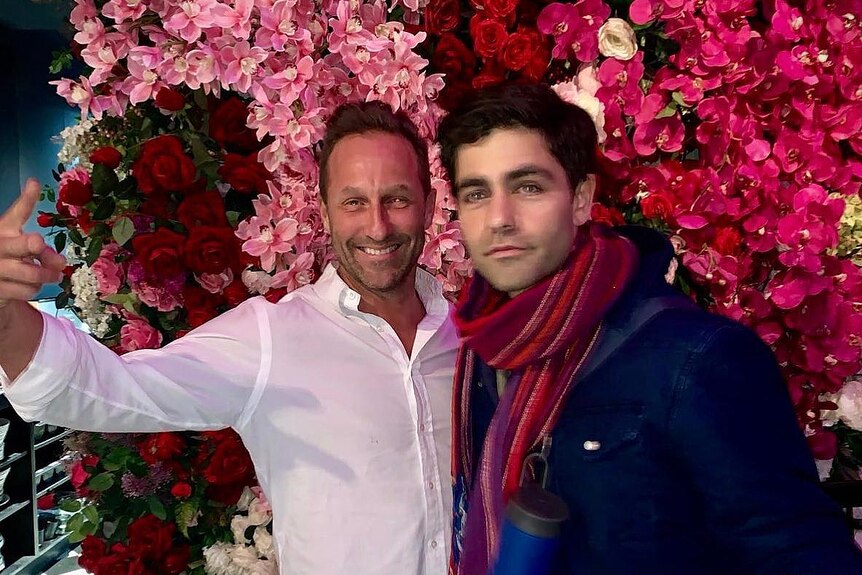 Two men posing in front of a flower wall