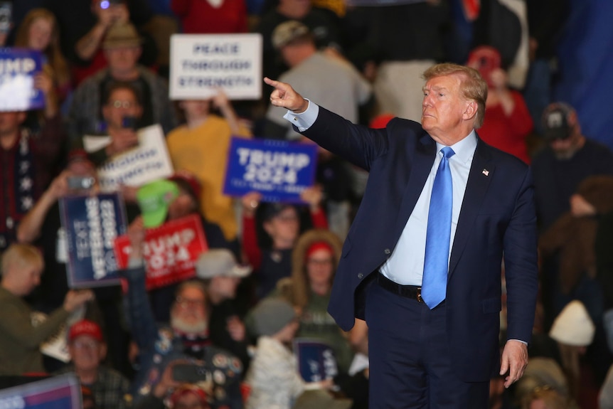 Donald Trump points at election rally with cheering fans and signs behind him