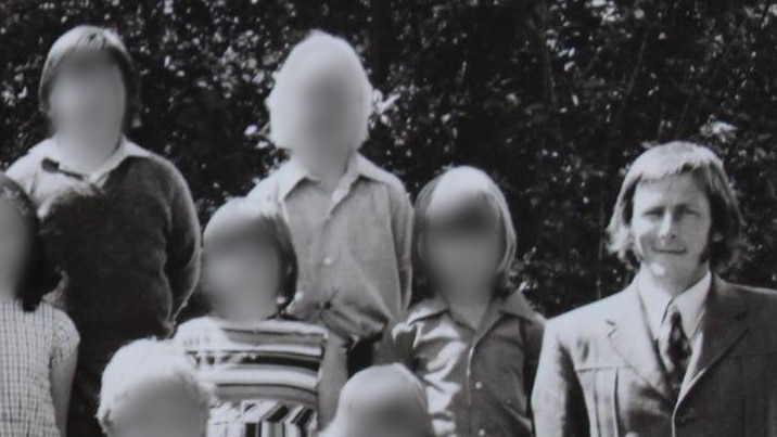 A black and white class photo with a male teacher. The children's faces are blurred.