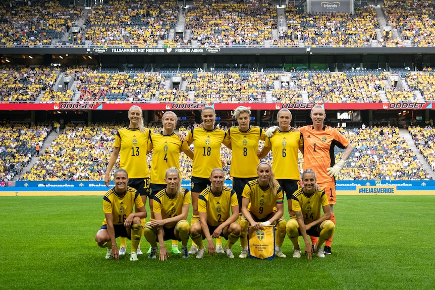 A women's soccer team wearing yellow and blue poses for a photo in front of a crowd