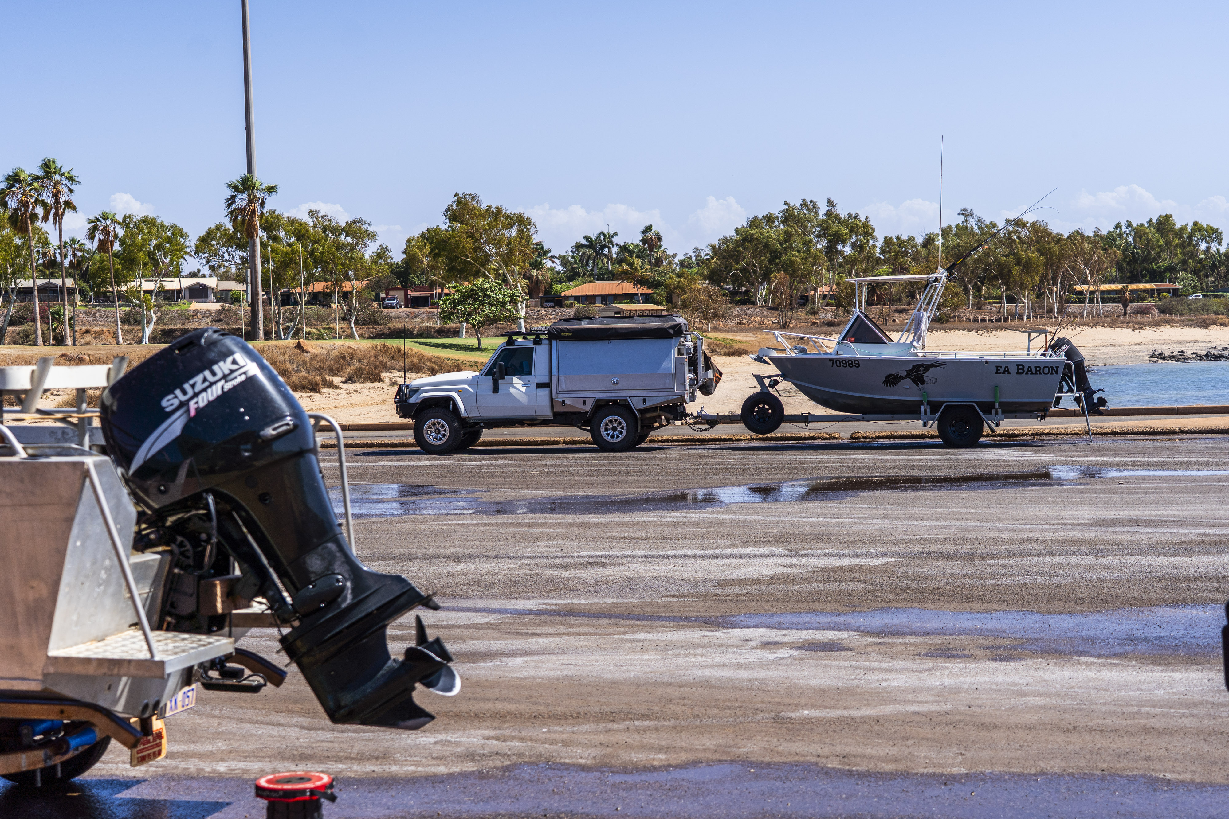 Um carro com um reboque e um barco à distância com um motor de barco em primeiro plano numa rampa para barcos.