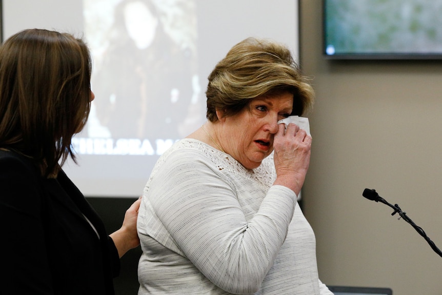 Donna Markham wipes her eyes with a tissue, while another woman puts a hand on her back.