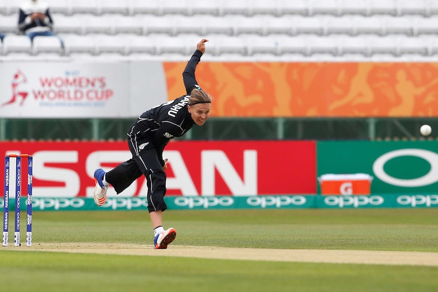 A female fast bowler follows through on her delivery as the ball flies through the air.