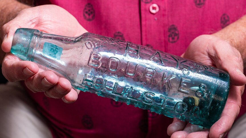 A man holding a glass bottle with the words Hay, Bourke and Hillston embossed on the side.