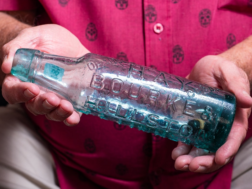 A man holding a glass bottle with the words Hay, Bourke and Hillston embossed on the side.