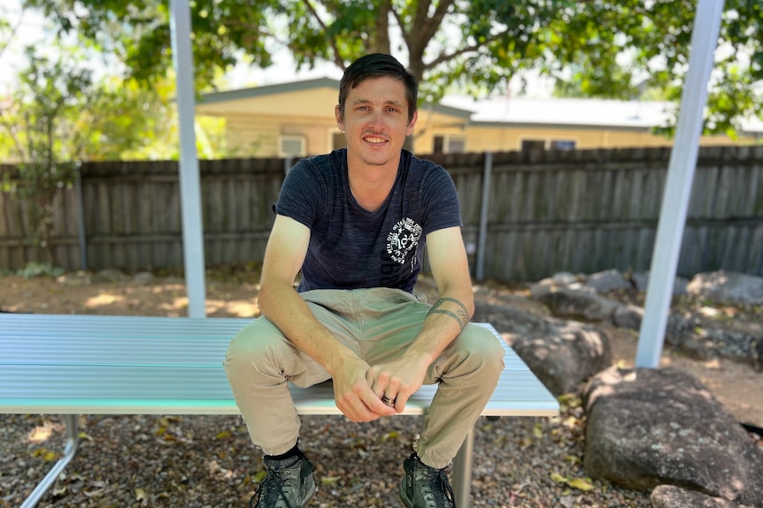 Bryce Dew sitting on a silver park bench. 