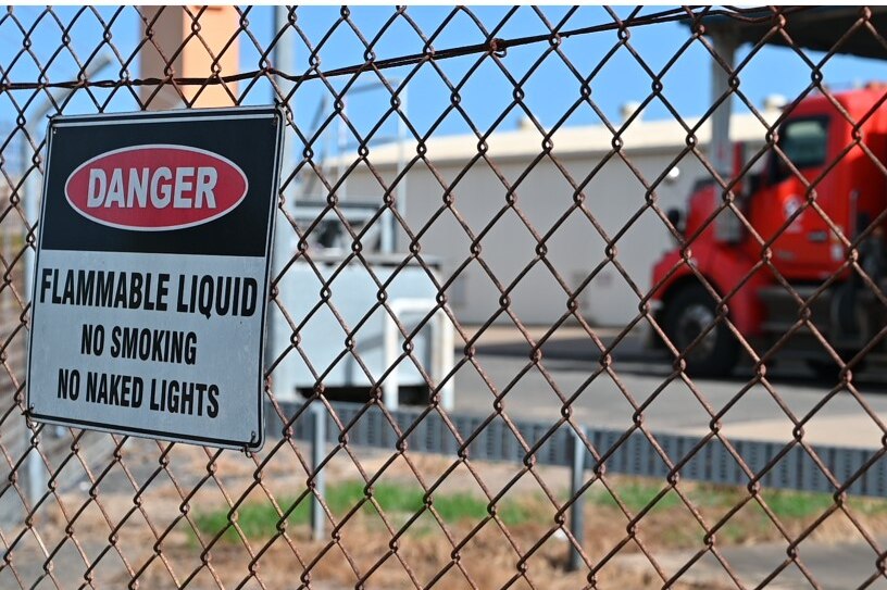 A danger sign hanging on a high wire fence reads flammable liquid in front of a petrol truck.