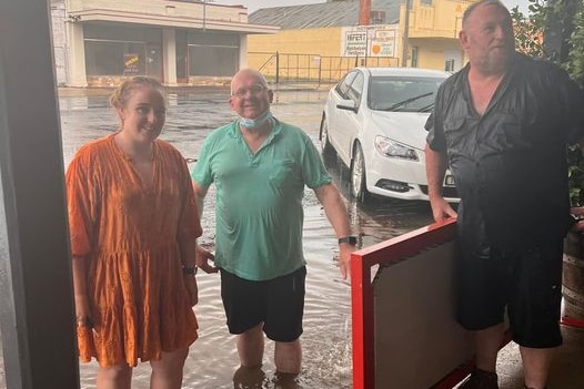 Three people stand on a flooded road on a rainy day.