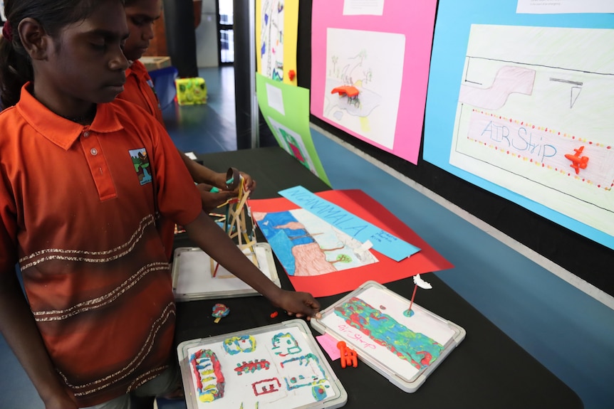 Two Aboriginal girls in school uniforms look at models made of plasticine 