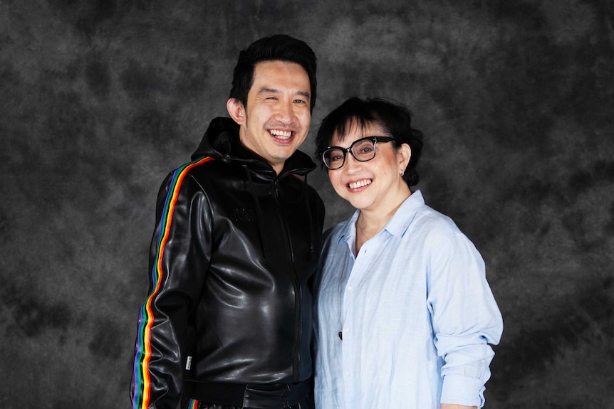 A man and his mum pose next to each other smiling at the camera. 