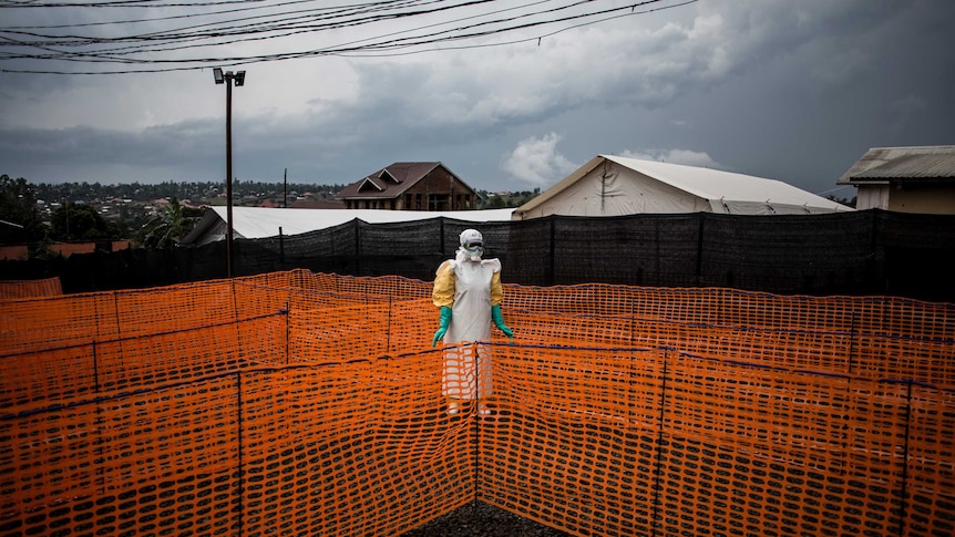 A health worker wearing Ebola protective equipment stands in the centre of bright orange barricades