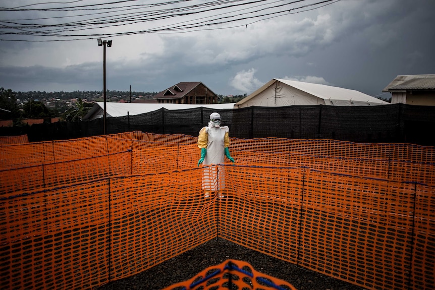A health worker wearing Ebola protective equipment stands in the centre of bright orange barricades