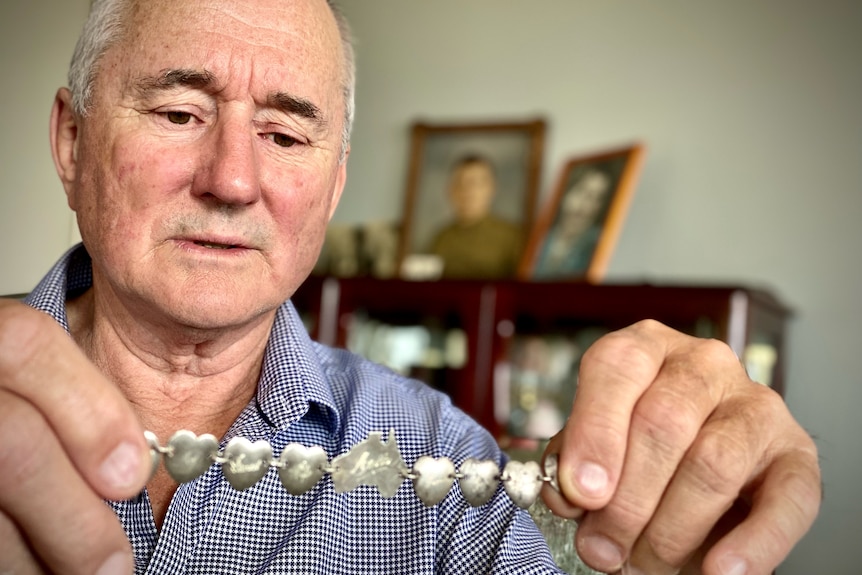 A man holds up a silver bracelet made up of heart shapes and the outline of Australia.