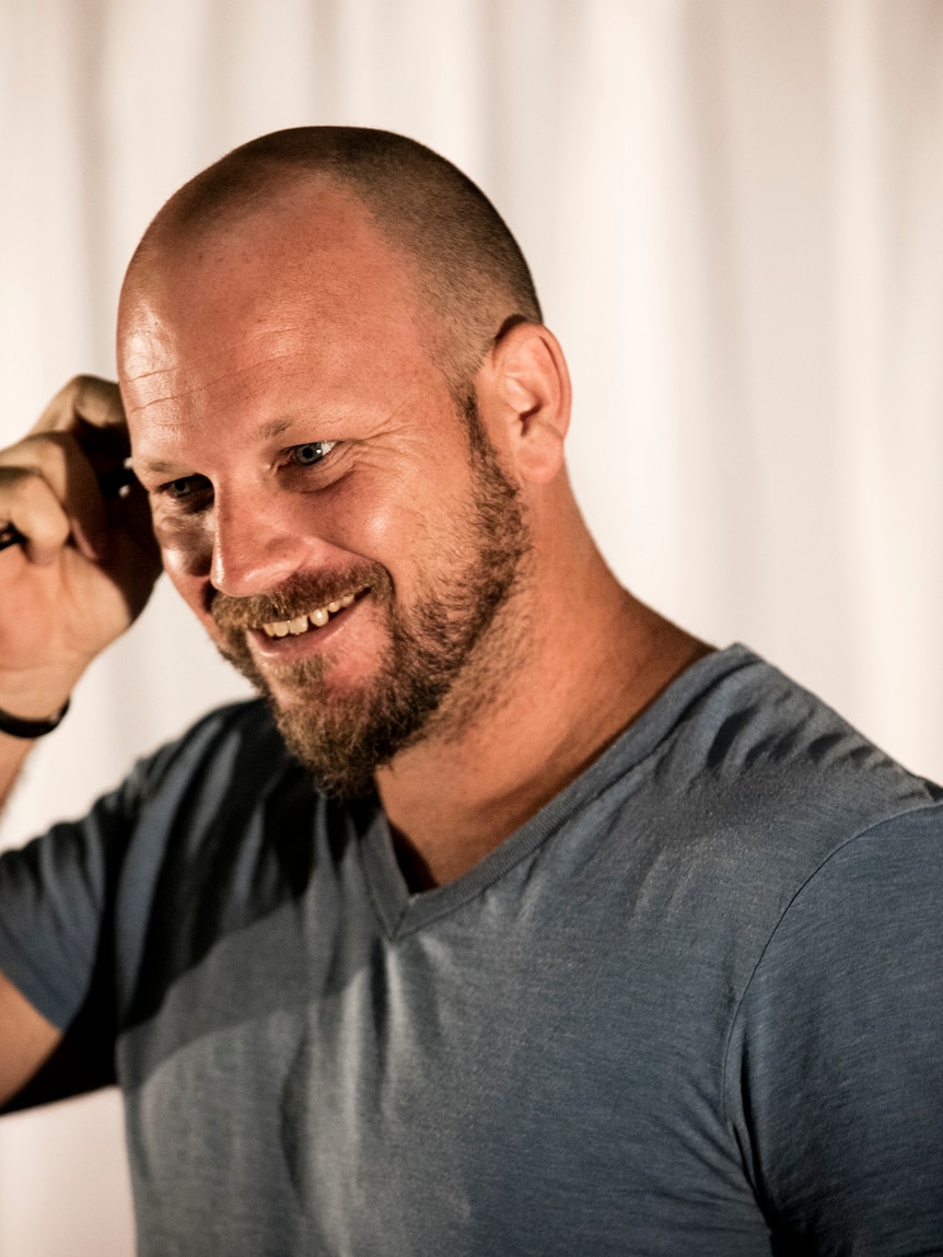 Colour portrait of director Josh Bond smiling away from the camera in front of white background.