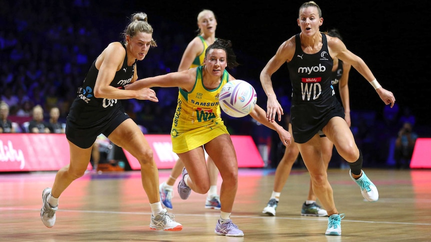 Three women netball players chase after a ball out in front of them.