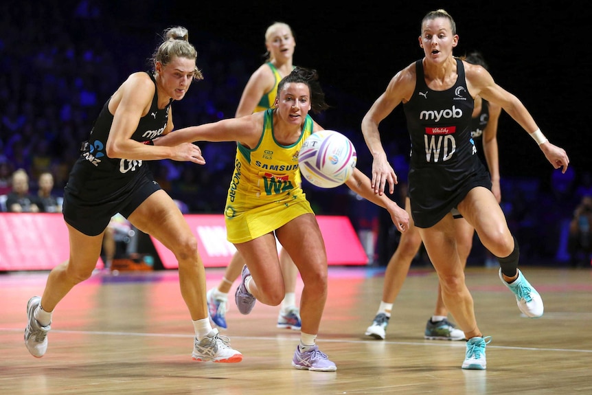 Three women netball players chase after a ball out in front of them.